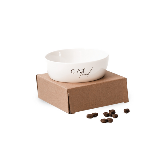 Ein weißer Keramiknapf mit dem Aufdruck "cat food" auf einem kleinen Karton vor einem weißen Hintergrund.