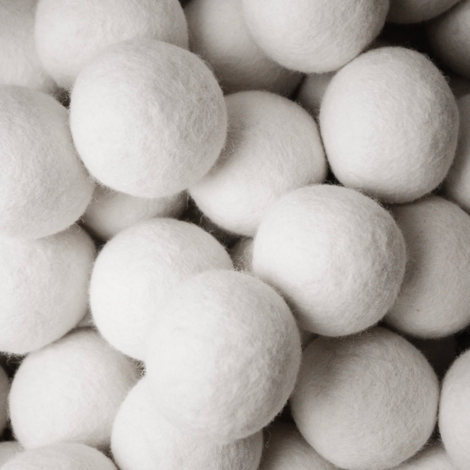 Hier zu sehen ist eine Nahaufnahme von einem Haufen ganz vieler Filzbälle in weiß, aus Schafswolle, für Katzen.