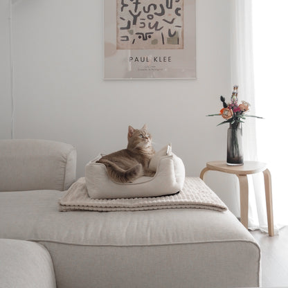 Eine Katze liegt in einem beigen Körbchen für Katzen in Leinenopritk für ein schönes Zuhause mit Katzen.