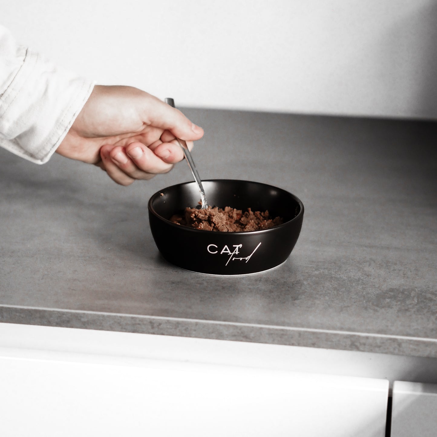 Nassfutter wird in einem schwarzen Katzennapf aus Keramik zur Fütterung der Fellnasen vorbereitet.