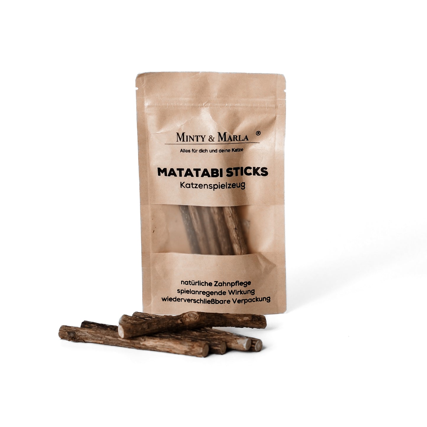 Eine braune Papierverpackung mit dem Aufdruck "Matatabi Sticks Katzenspielzeug" der Marke Minty & Marla  steht vor einem weißen Hintergund. Vor der Verpackung liegen kleine Hölzer, welche Matatabi Sticks heißen und als Spielzeug für Katzen dienen.